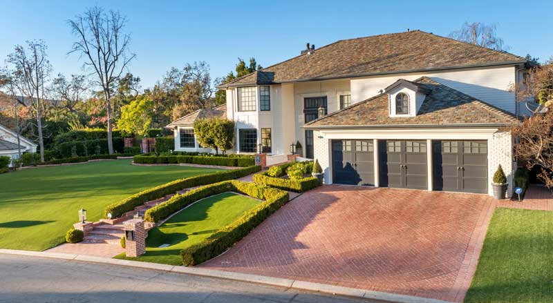 Red brick driveway and matching front steps with manicured hedges framing the walkway, highlighting a luxury entryway
