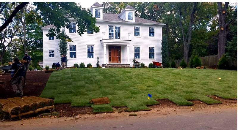 Workers have nearly completed installing sod in the front yard of a large historic home