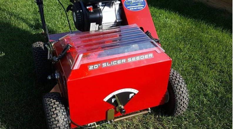 A red lawn care slicer-seeder machine is shown planting grass seeds on a lawn