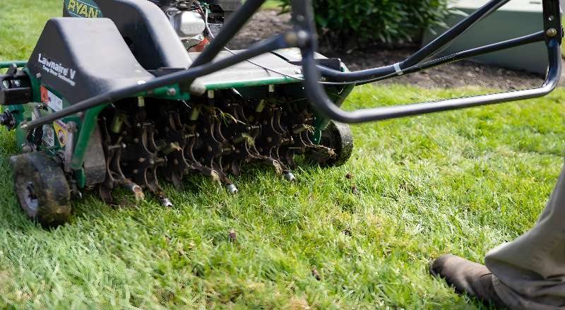 A landscape professional is using a lawn aerator machine to prepare the grass for seeding