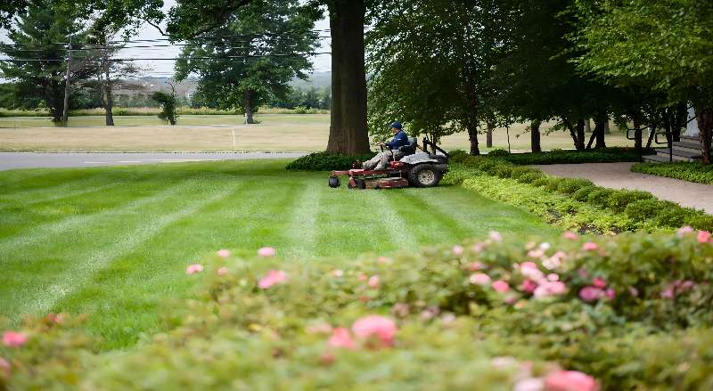 A landscape worker uses a riding lawn mower to cut the grass of a large property