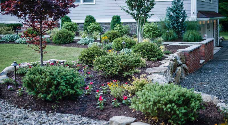 Natural stone retaining wall with integrated plantings and flower beds, adding elevation and character to a front yard landscape