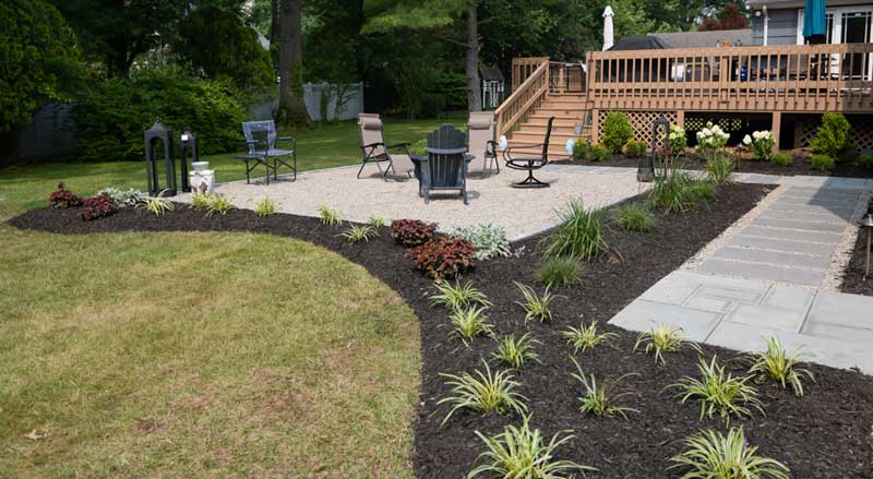 A backyard with new plantings, a patio, and wooden deck