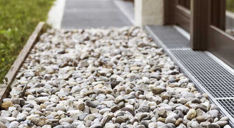 close-up of drain near foundation of home surrounded by decorative rocks