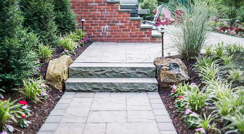 Hardscaped patio, steps, and walkway lined with garden beds
