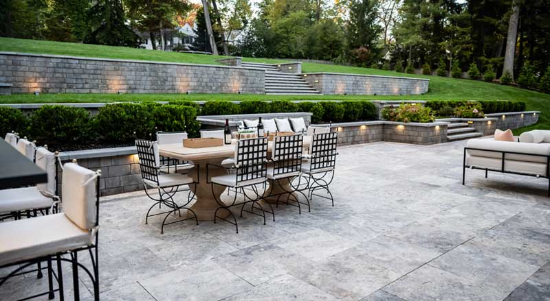 Hardscaped outdoor patio with dining furniture, tiered stone retaining walls, and built-in lighting in a New Jersey backyard