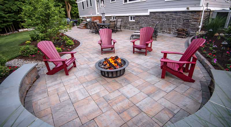 Bluestone patio with red Adirondack chairs around a fire pit, blending outdoor living space with landscaped garden beds