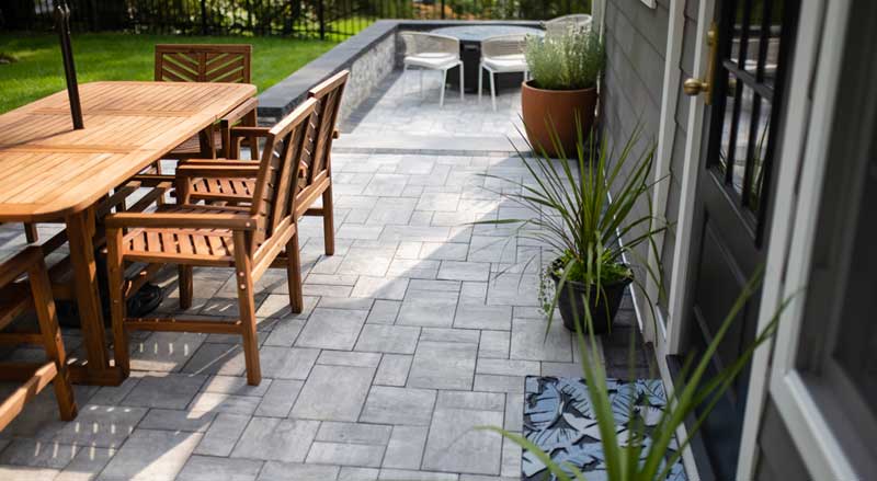 Modern New Jersey backyard patio with stone pavers, wood dining furniture, and potted plants creating a welcoming outdoor living space