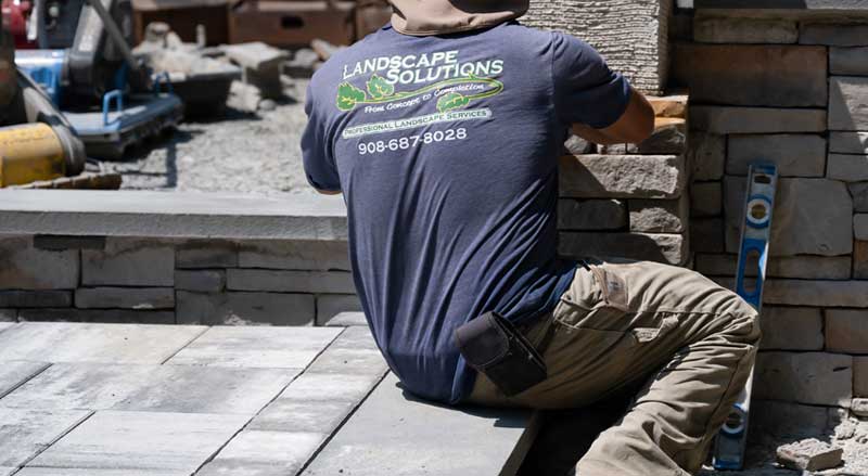 Landscape Solutions crew member building a custom stone patio and retaining wall in New Jersey
