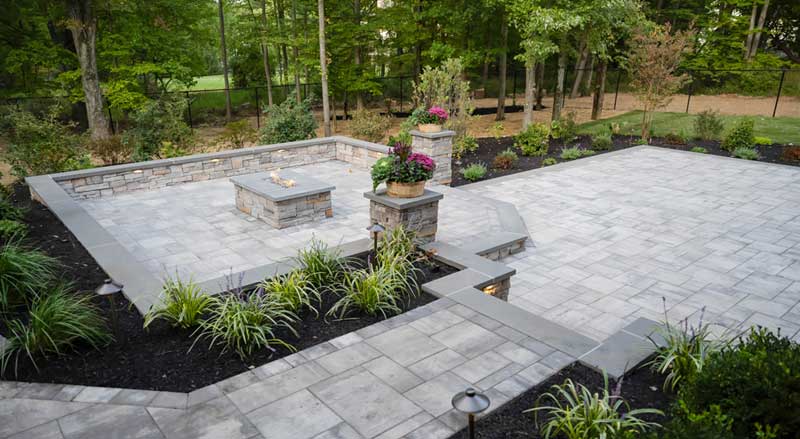 A multi-level backyard patio with bluestone accents and a fire table