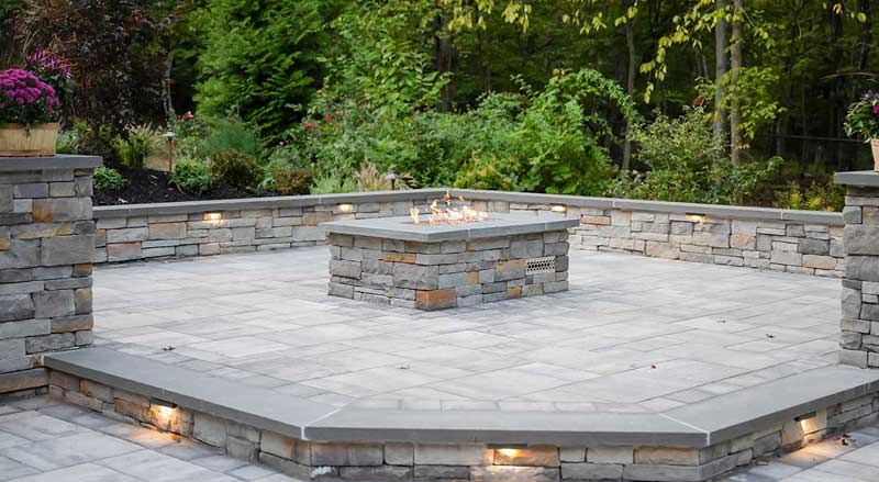 Contemporary stone fire pit with built-in seating and ambient lighting, reflecting the rising popularity of cozy gathering spaces in NJ landscapes.