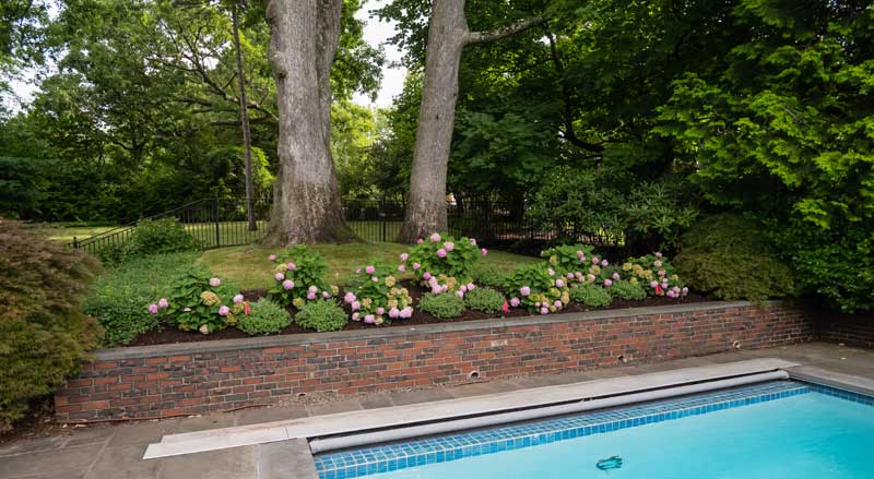 A landscaped yard with pool, flowers, and retaining wall