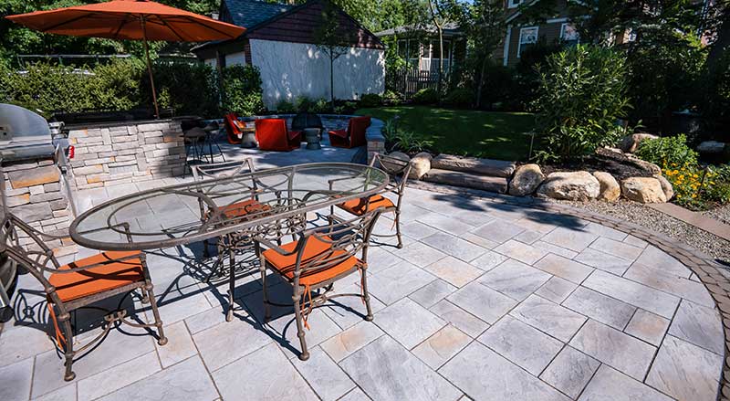 Multicolor curved paver patio design with border, bar, grill, and dining table