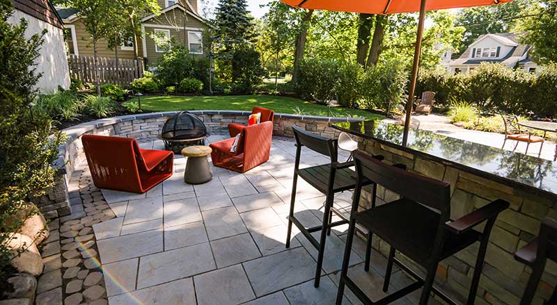 Curved patio with firepit and sitting wall, an outdoor bar, and a separate area for table dining.