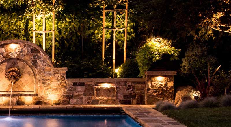 Outdoor lighting and a water feature enhance a backyard landscape