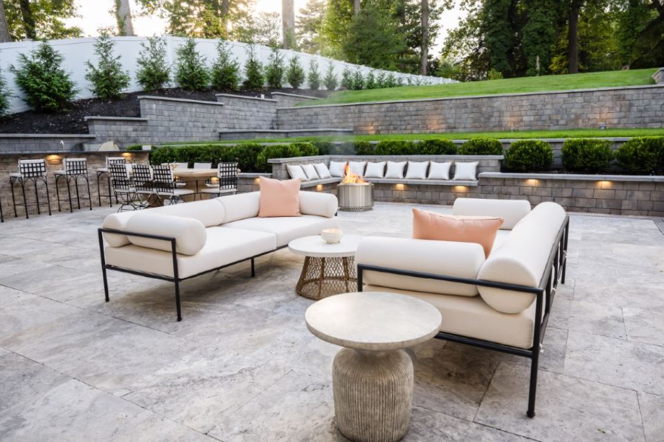 Custom stone patio with built-in seating walls, retaining walls, landscape lighting, and outdoor fire feature designed for summer entertaining