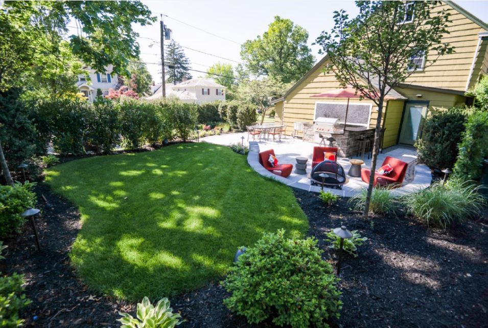 Mature landscape featuring healthy lawn, ornamental shrubs, privacy hedges, and colorful plantings surrounding a custom backyard patio
