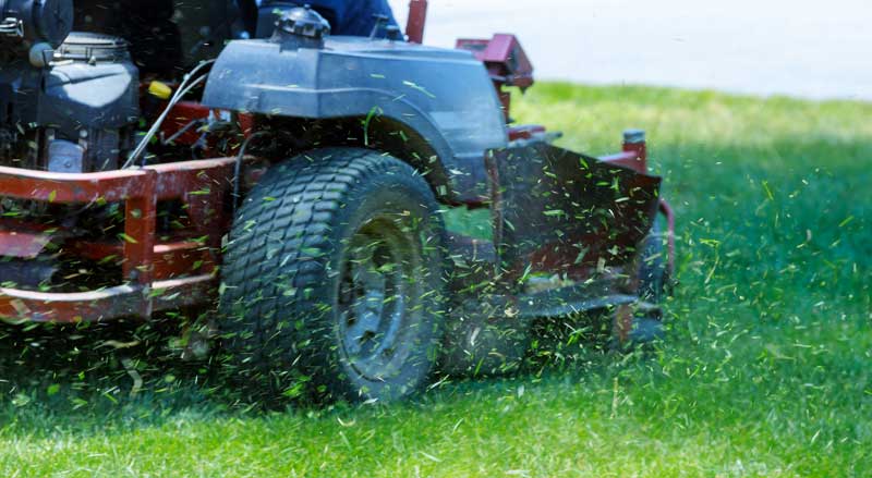 A riding lawnmower with grass clippings flying around it