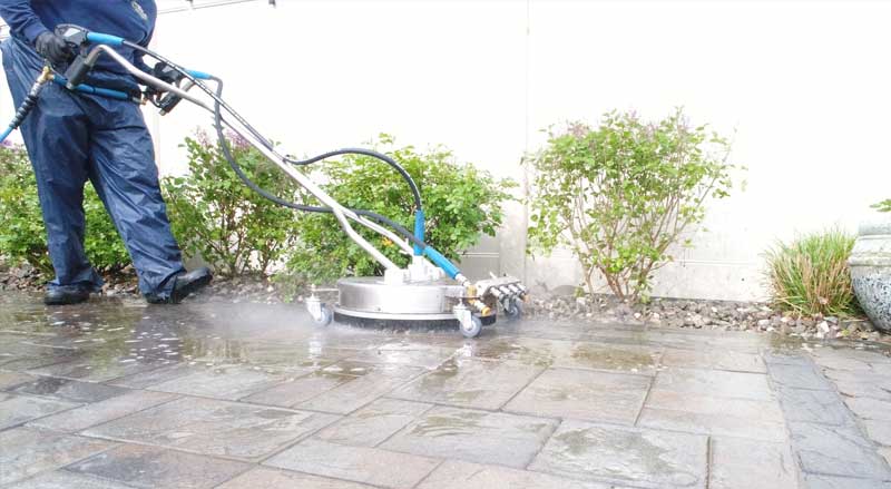 A man with a power washing machine cleaning a stone paver patio