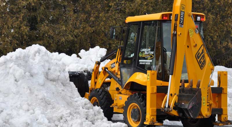 Snow removal equipment clearing large piles of snow during winter property maintenance under a full-service landscape management plan