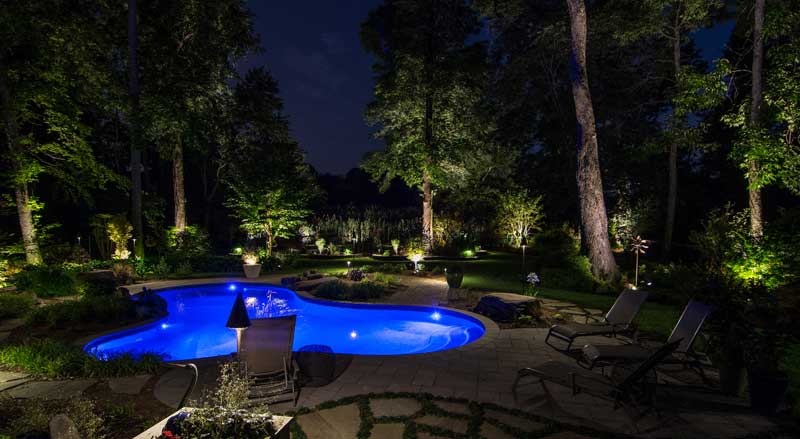 An inviting backyard with a glowing pool, enhanced by elegant lighting