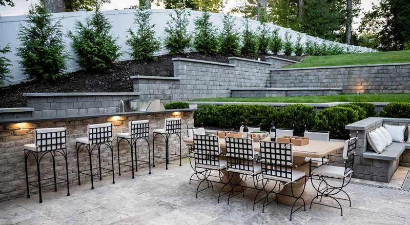 Multi-level hardscape patio featuring an outdoor kitchen, bar seating, and retaining walls