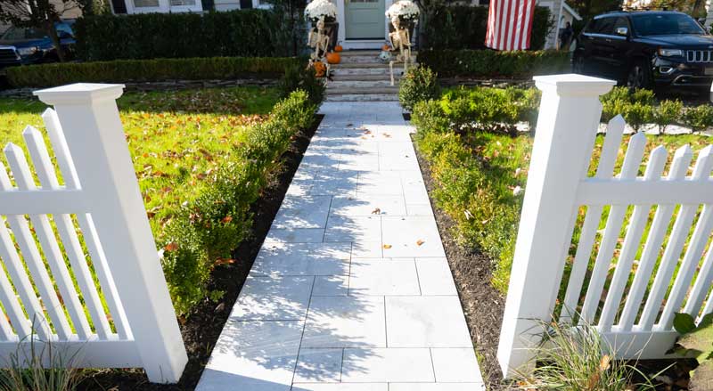 Front yard walkway with white picket fence and manicured hedges, demonstrating finished hardscape and landscape design