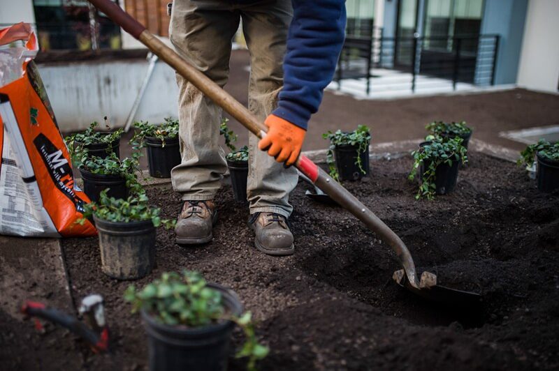 A Landscape Solutions worker uses a shovel to dig a hole, emphasizing the importance of seasonal property maintenance and preparation