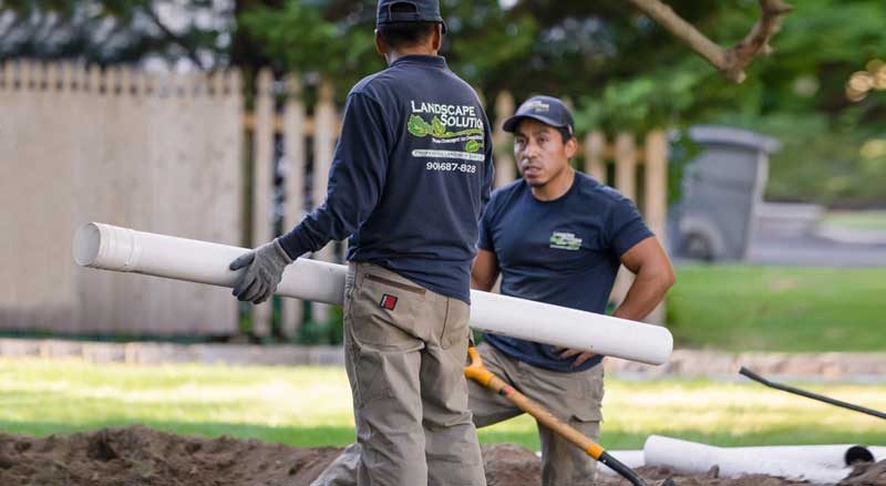 Professional landscaping crew installing drainage materials during a permitted project