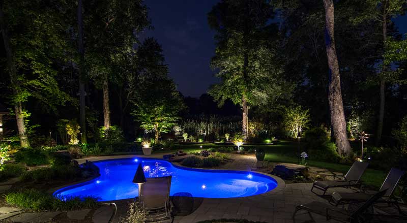 Beautifully lit backyard pool and landscape at night