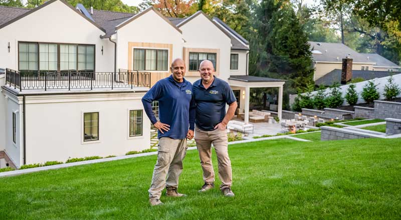 Two professional landscapers standing proudly in front of a well-maintained residential property