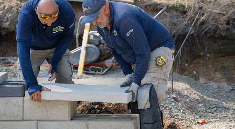 Landscape crew installing stone steps and hardscape features during active construction phase