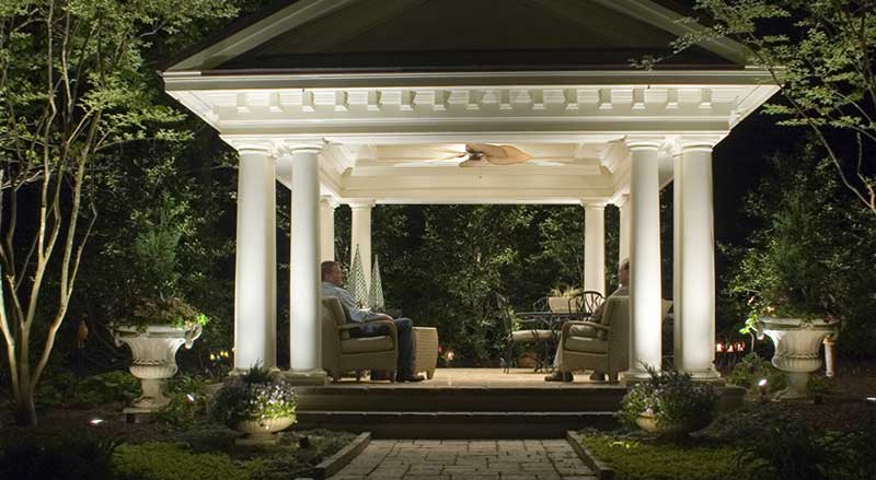 A furnished, beautifully illuminated gazebo and walkway lit up at night