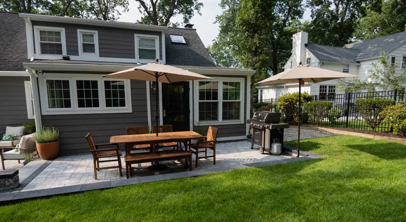 Backyard patio with outdoor dining area and grill, showing a finished hardscape project ready for summer use