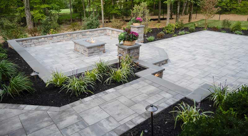 Expansive paver patio with fire pit, raised planters, and stone walls