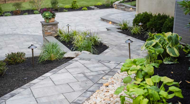 Paver patio and walkway installation with landscape lighting and fresh plantings during peak landscaping season