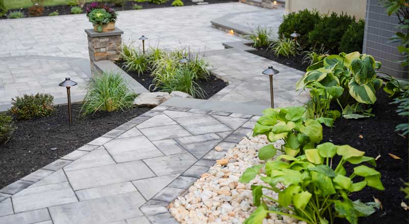 Stone paver walkway and garden beds with landscape lighting and fresh spring planting